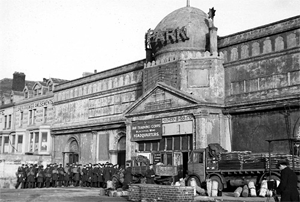 Black and white photo of people and lorries outside a large, weathered building labelled "BATHS," serving as a training corps headquarters.