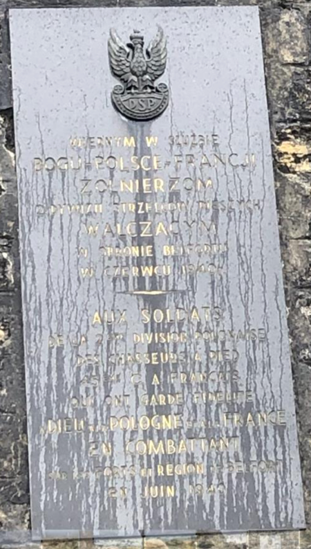 A metal plaque on a stone wall commemorates Polish soldiers who fought in the Battle of Belfort, with inscriptions in Polish, French, and a military emblem at the top.