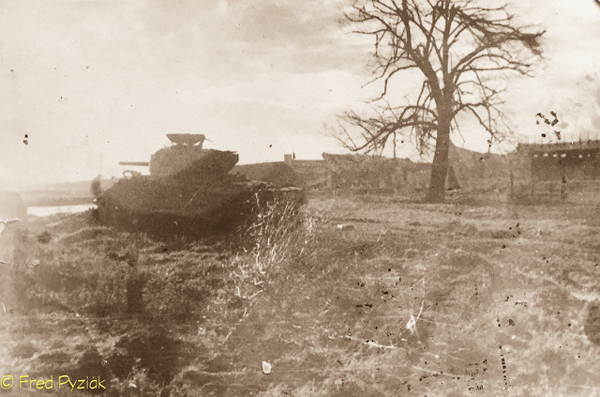 Sepia-toned photo of an abandoned tank in a desolate field with a leafless tree and a few buildings in the background.