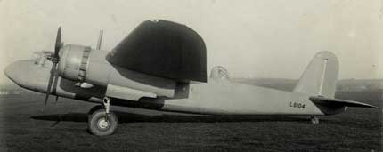 Side view of a vintage twin-engined aeroplane on grass, featuring a large, unusual black dome covering the cockpit area.