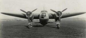 Front view of a twin-engined vintage aeroplane with a propeller on each wing, parked on a grassy field.