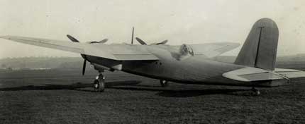 Black and white photo of a twin-engined military aeroplane parked on grass, viewed from the rear side under overcast skies.