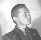 Black and white portrait of a man in a suit and tie, facing left, with short hair, photographed against a plain background.