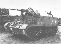 A vintage military tracked vehicle with soldiers on board, equipped with mounted machine guns, is parked on a field.