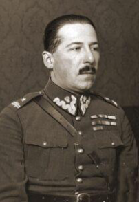A man in a military uniform with medals and decorations, sitting for a formal portrait against a plain patterned background.