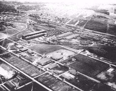 Aerial black-and-white photo showing a large complex of buildings, open fields, and roads, with vehicles and structures arranged in an organised layout.
