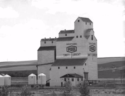 A large grain elevator labelled "Saskatchewan Pool Swift Current" stands on flat land with several smaller storage silos nearby.