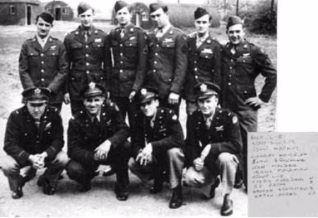 Black-and-white photo of ten men in military uniforms posing outdoors, with three crouching in front and seven standing behind; handwritten note visible in the bottom right-hand corner.