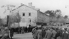 A black and white photo shows a crowd gathered outside the entrance of Camp de Courtoisville, with a large building and trees in the background.