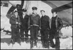 Five men in military uniforms stand in the snow in front of an aeroplane.