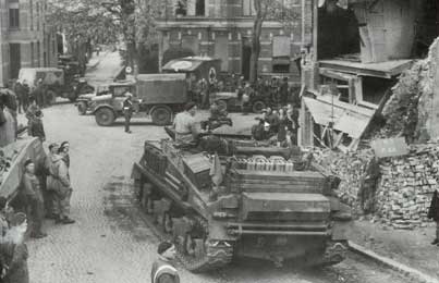 Military vehicles and soldiers occupy a damaged urban street; a building shows significant structural damage, with debris piled nearby and people observing the scene.