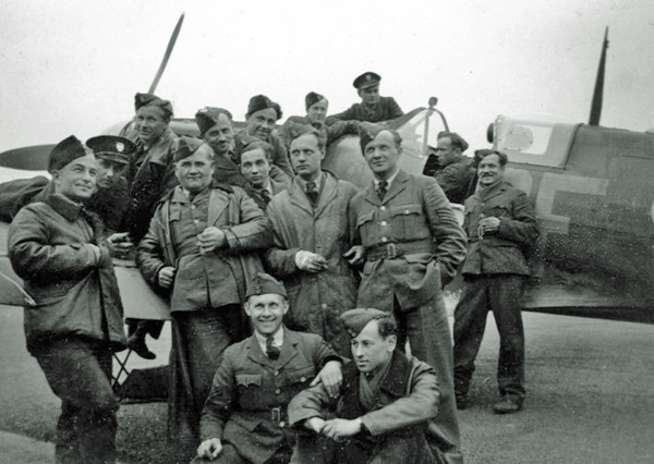A group of Second World War-era soldiers in uniform pose in front of a military aeroplane on an airfield.