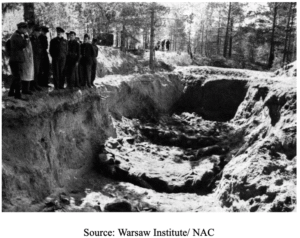 A group of people stands at the edge of a large mass grave in a forested area; partially buried bodies are visible in the pit.