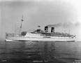 Black and white photo of a large ocean liner with two smokestacks, sailing on calm water under a clear sky.