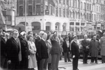 A group of people, including uniformed officers and civilians, stand in a row on a city street during a formal outdoor event.
