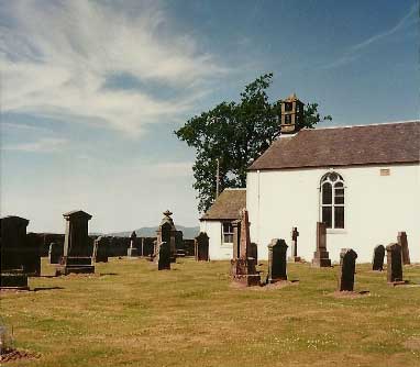 A small graveyard with old headstones beside a white church building under a blue sky with scattered clouds.
