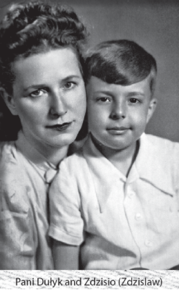A woman with short, wavy hair sits close to a young boy with a side-parted haircut; both wear light-coloured shirts and look at the camera.