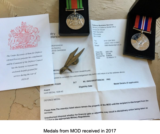 Two military medals, a badge, and official Ministry of Defence letters confirming award details are arranged on a table.