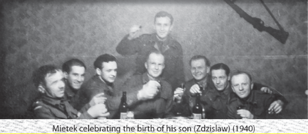 A group of eight men in military uniforms sit and stand around a table with drinks, raising glasses in a celebratory toast.