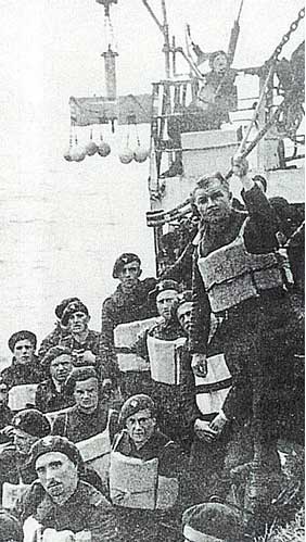 A group of soldiers wearing life jackets gather on the deck of a ship, with some standing and others seated, preparing for an operation.