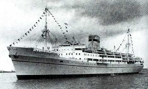Black and white photo of a large passenger ship decorated with signal flags, docked on calm water under a cloudy sky.