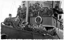 A group of uniformed men pose on the deck and upper level of a ship, facing the camera.