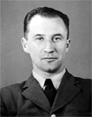 Black and white portrait of a man in a suit and tie, facing the camera and displaying a neutral expression.