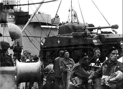 Military personnel and a tank are seen on the deck of a ship, with various crew members standing and observing the surroundings.