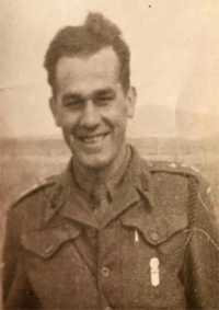 A man in a military uniform smiles at the camera in a sepia-toned photograph, with an open field in the background.