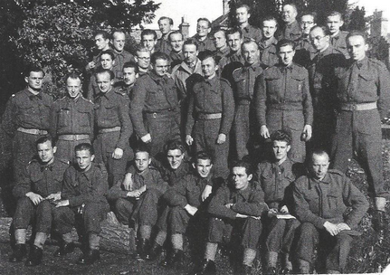 A group of soldiers in uniform pose outdoors for a black and white group photograph, with some sitting and others standing.