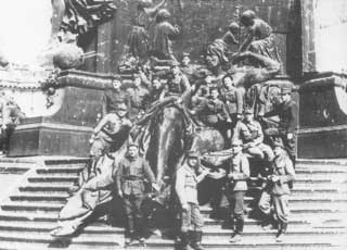 A group of soldiers pose on the steps of a large monument featuring human figures in relief.