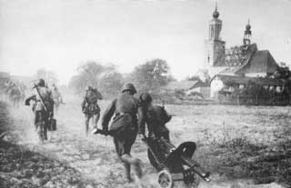 Soldiers running across a dirt road carrying equipment, with a church and buildings visible in the background. The scene appears historical and wartime.
