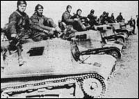A black-and-white photo shows soldiers sitting on top of several lined-up military tanks, likely from a historical wartime setting.