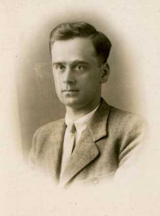 Black and white portrait of a young man wearing a suit and tie, looking slightly to the side with a neutral expression.