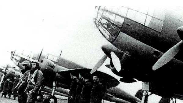 Black and white photo showing military personnel standing in front of large propeller aeroplanes lined up on a runway.