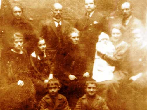 Sepia-toned, old photograph of a family group with adults, children, and a baby, all posed and looking at the camera.