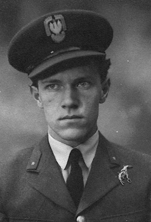 A young man in a military uniform and cap with an emblem, looking straight ahead with a serious expression.