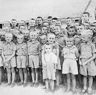 A group of boys in uniform pose for a photo outdoors, with one smaller child standing at the front.