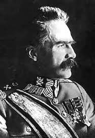 A man in a military uniform with medals and decorations looks to the side against a dark background.
