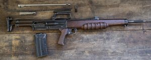 A partially dismantled vintage rifle with a wooden stock and metal parts laid out on a wooden surface.