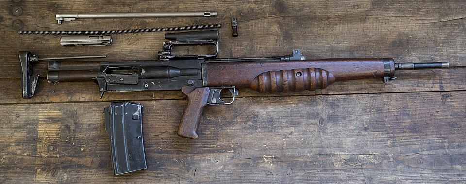 A partially dismantled vintage rifle with a wooden stock and metal parts laid out on a wooden surface.