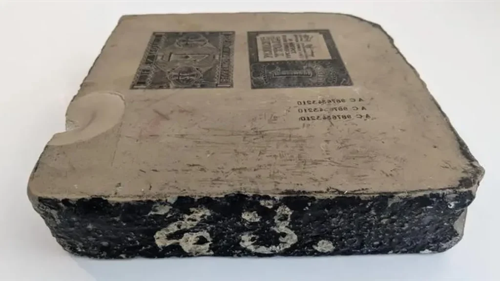 A rectangular lithography stone with labels and markings on the top surface; one corner is chipped, revealing the stone’s texture.